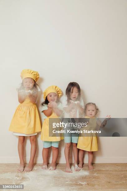 four little asian girls in a yellow apron and a chef's hat sprinkled flour - baby spielt mit essen stock-fotos und bilder