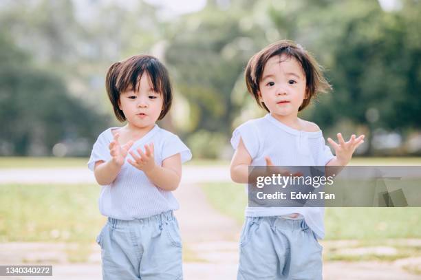 cute asian chinese twin baby boys looking curiously at lawn public park - cute twins stockfoto's en -beelden