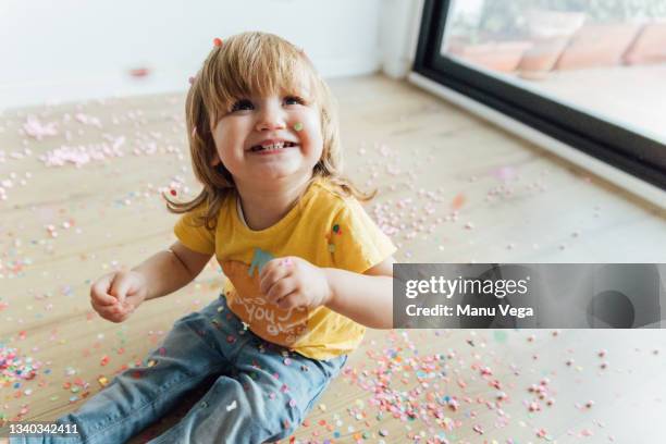 from above of cheerful infant child sitting on floor and throwing up colorful sprinkles and confetti while having fun celebrating in nursery. - messy house after party bildbanksfoton och bilder