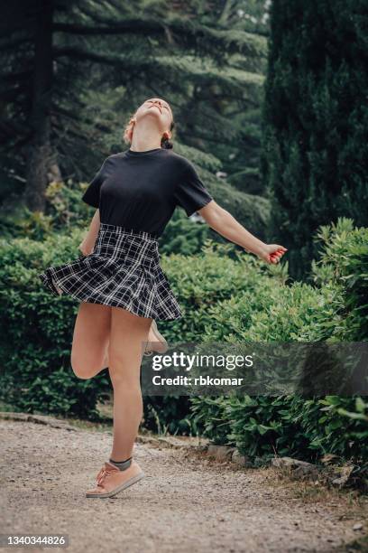 happiness of a female teenager spinning on one leg outdoors - girls in plaid skirts stock pictures, royalty-free photos & images