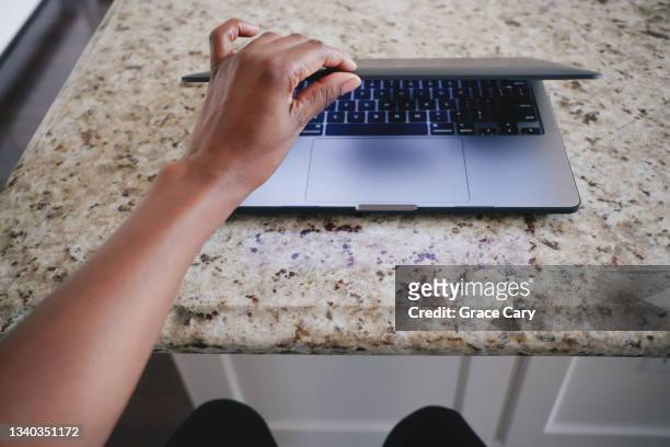 woman sits at kitchen island to work on laptop - open laptop stock pictures, royalty-free photos & images