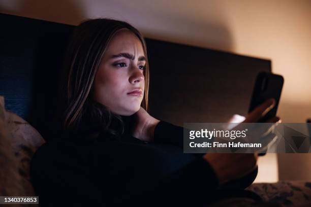 bad news young woman reading messages on mobile phone lying in bed at night - suspicion stock pictures, royalty-free photos & images