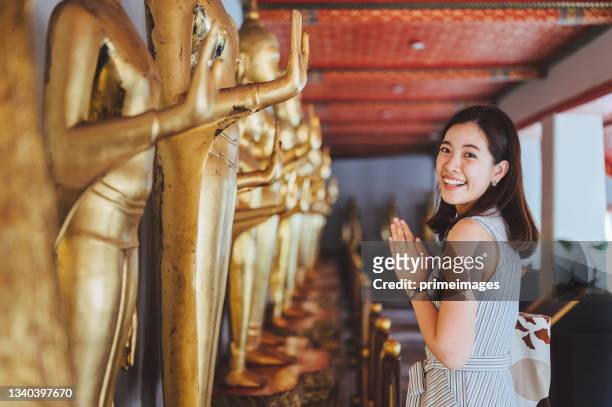 relaxing moment weekend thai /chinese young asian tourist joyful woman doing sawasdee (pray) traveling praying at statue at wat pho temple bangkok, thailand - 泰國人 個照片及圖片檔