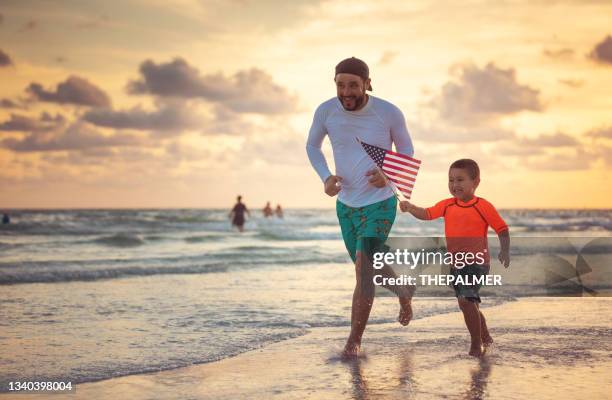 father and son running with an american flag on the beach - beach florida family stockfoto's en -beelden