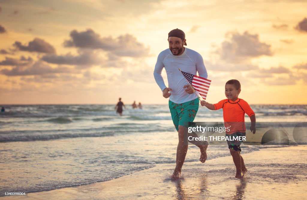 Pai e filho correndo com uma bandeira americana na praia