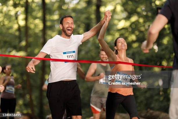 happy athletic couple crossing the finish line during marathon in nature. - marathon runner finish line stock pictures, royalty-free photos & images
