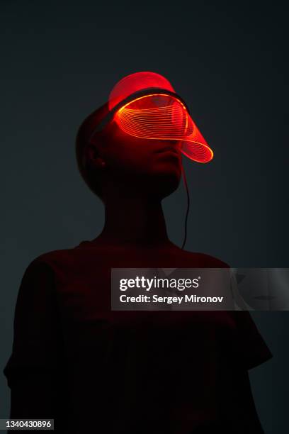 futuristic sot of young woman wearing led beauty mask with red lights over dark background - future health care stock-fotos und bilder