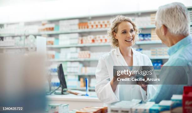 cropped shot of an attractive young chemist helping a senior male customer in her pharmacy - pharmacy stockfoto's en -beelden