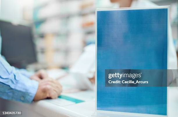 closeup shot of a sign on the counter of a chemist while an unrecognizable pharmacist and customer talk in the background - commercial sign stockfoto's en -beelden