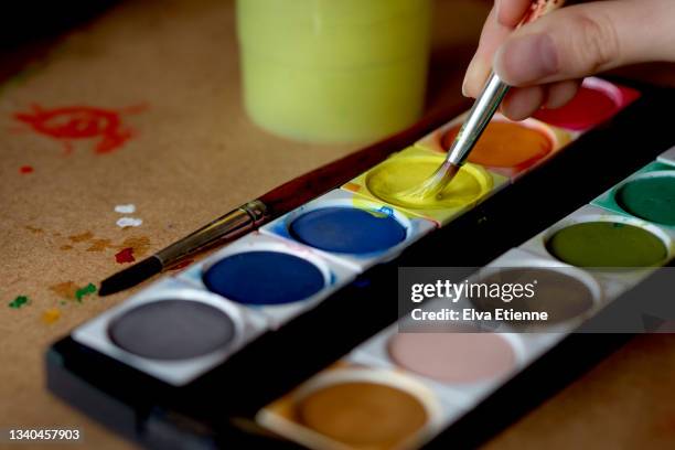 close up of a paintbrush being loaded up with yellow paint from a multicoloured paint palette by a teenager - making art stock pictures, royalty-free photos & images