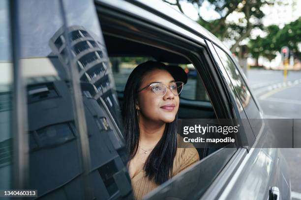 smiling young woman looking at the city from the backseat of a taxi - driver rider stock pictures, royalty-free photos & images