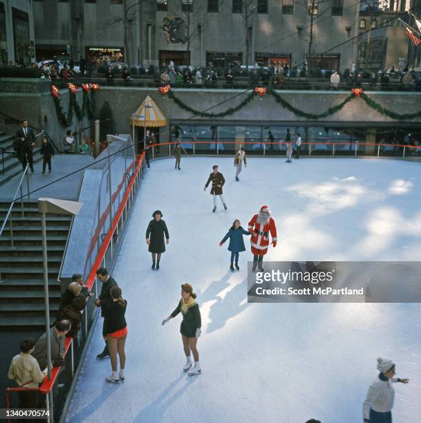 Elevated view of people, including one dressed as Santa Claus, as they skate on the ice rink at Rockefeller Center, New York, New York, December 1969.