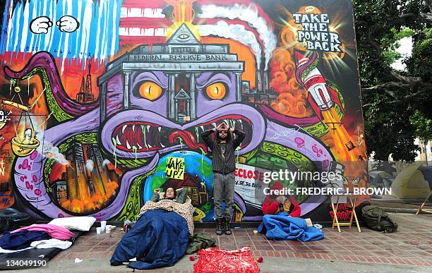 Campers stay comfortable as another gestures in front of a graffiti-strewn wall at the Occupy LA site in front of City Hall in downtown Los Angeles...