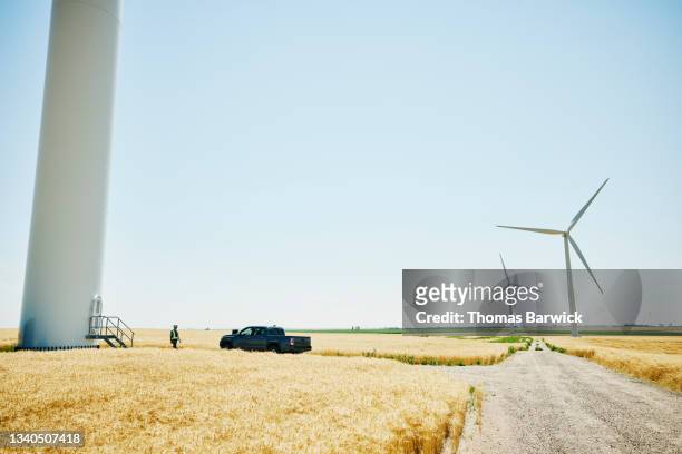 Extreme wide shot of engineer preparing to inspect wind turbine on summer afternoon