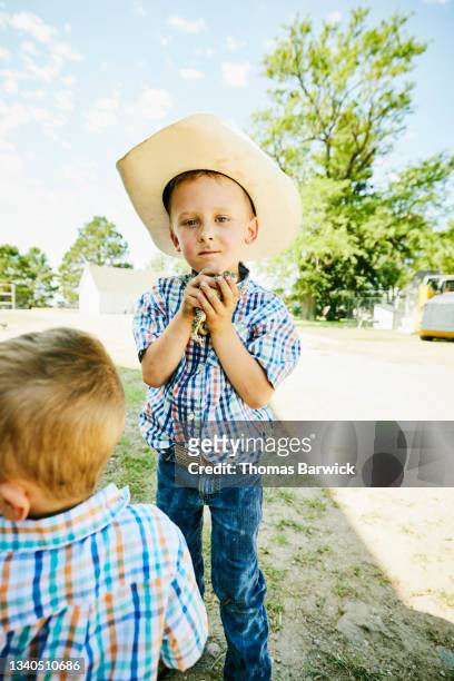 Wide shot of young boy holding toad on farm on summer morning