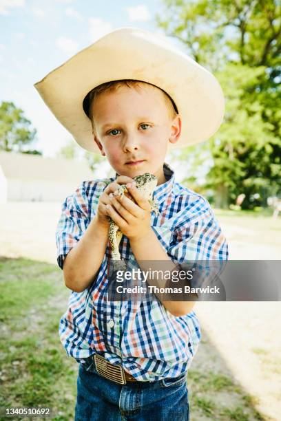 Medium wide shot of young boy holding toad on farm on summer morning