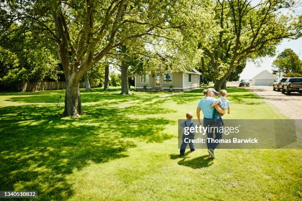 wide shot rear view of grandmother walking with grandsons through front yard of home - beautiful granny stock-fotos und bilder