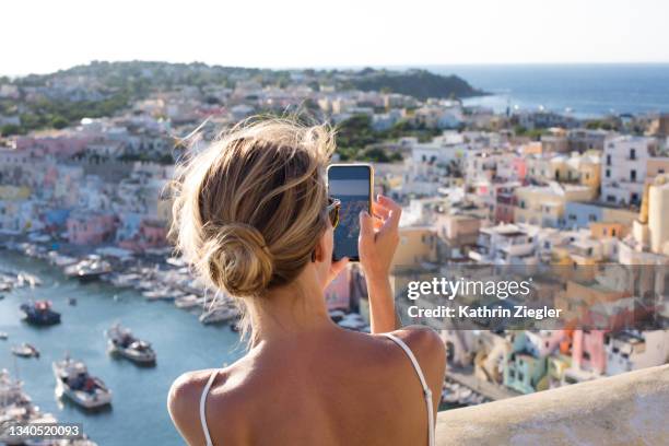 woman taking pictures of the idyllic port of corricella, procida island, italy - turism stock-fotos und bilder