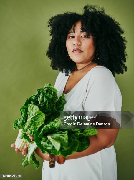 studio shot of a young woman holding a bunch of spinach against a green background - curvy black women stockfoto's en -beelden