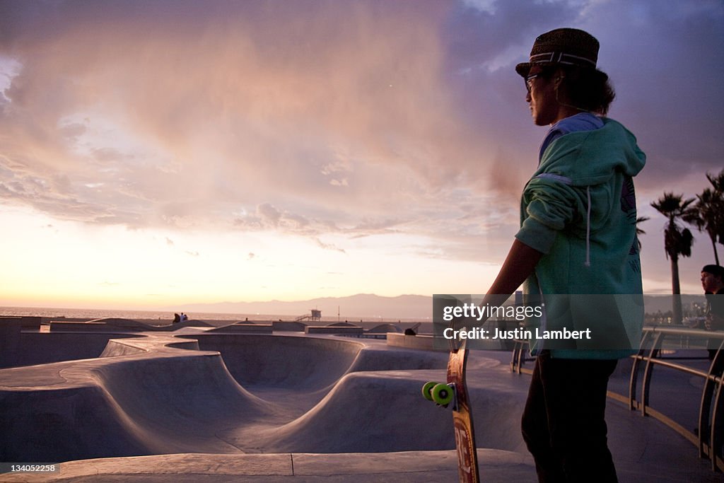 MAN STANDS LOOKING AT SKATE PARK IN SUNSET L.A