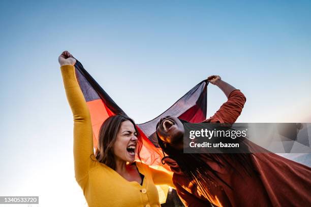 two multi-ethnic women holding german flag - germany celebrates reunification day stock pictures, royalty-free photos & images