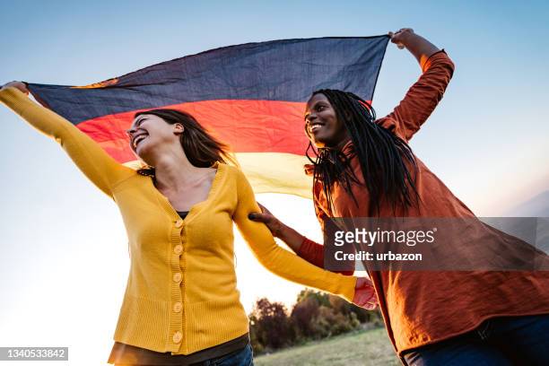 two multi-ethnic women holding german flag - germany celebrates reunification day stock pictures, royalty-free photos & images