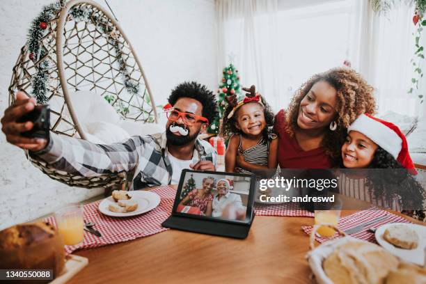 two generations of family celebrating christmas at home and video conferencing with grandparents, maintaining social distance - african ethnicity christmas stock pictures, royalty-free photos & images