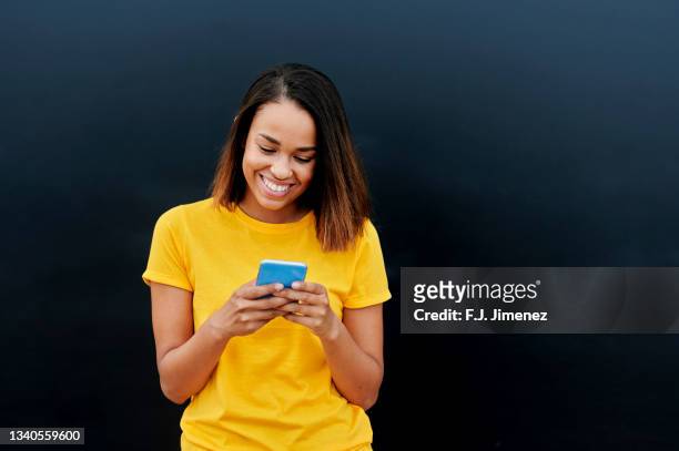 woman in yellow t-shirt using smart phone - black t shirt stock pictures, royalty-free photos & images