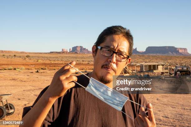 young navajo man in his twenties portrait while wearing or putting on his covid-19 coronavirus mask to flatten the curve and stop the spread during the pandemic on a sunny late afternoon - labor camp bildbanksfoton och bilder