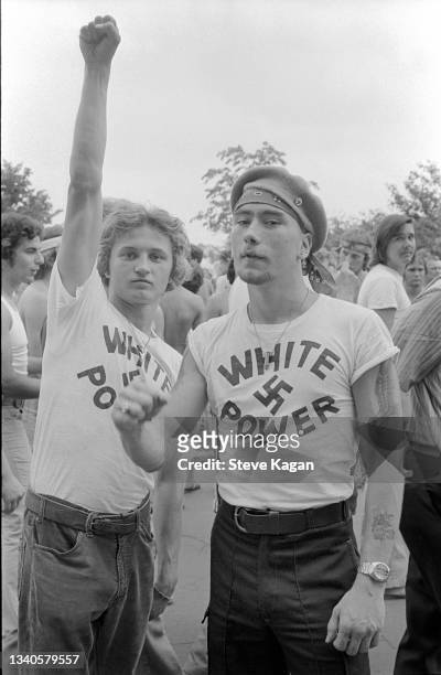 View of two young men, one with a raised fist, participate in a neo-Nazi march, Chicago, Illinois, July 1978. Both wear t-shirts that read 'White...