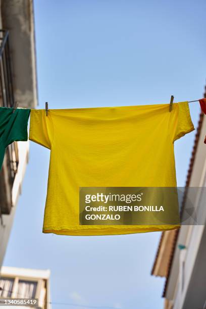 clothesline with yellow t-shirt between houses hanging by clothespin on blue sky background. - closet shelf of colorful folded clothes stockfoto's en -beelden