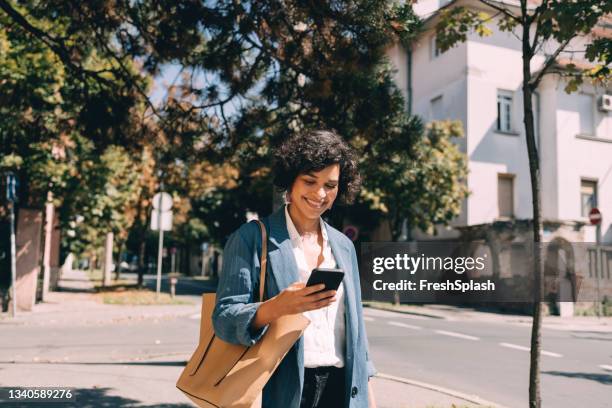 beautiful woman using mobile phone outdoors - woman walks down street stock pictures, royalty-free photos & images