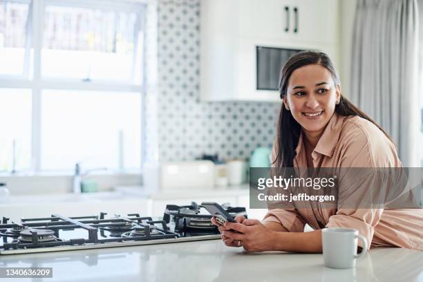 shot of an attractive young woman leaning on her kitchen counter at home and using her cellphone - cooker dial stock pictures, royalty-free photos & images