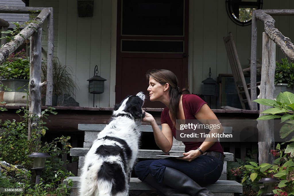 Woman holding digital tablet as she kisses dog