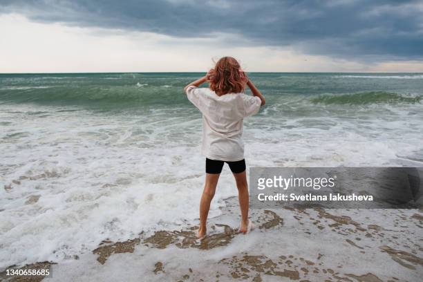 atmospheric photo of a pink-haired girl standing on the shore of a stormy sea in summer cloudy weather with dramatic clouds - thunderstorm ocean blue stock-fotos und bilder