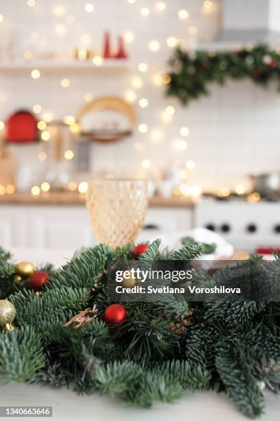 white kitchen interior with christmas decorative composition of spruce sprigs decorated wooden deer figure, red and golden ball toys on it on the festive table on the foreground - christmas toys wooden background foto e immagini stock