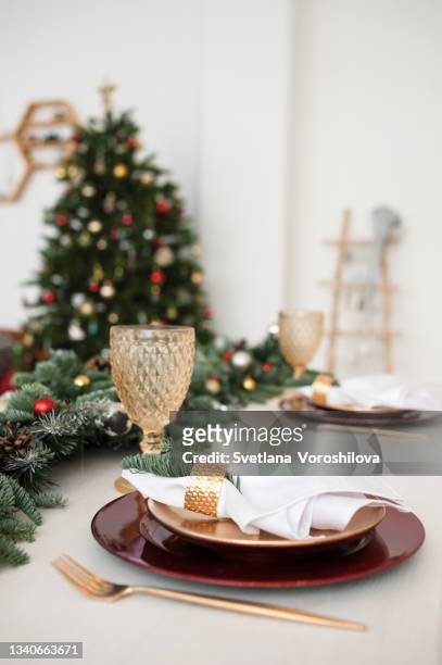 festive christmas table setting with decor of the spruce sprigs, golden kitchen utensils, red plates and christmas tree on the background. - food decoration stock-fotos und bilder
