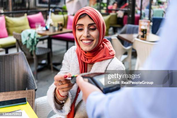 muslim mature woman paying for cafe by credit card reader - customers pay with contactless cards imagens e fotografias de stock