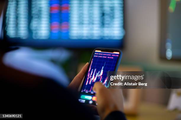 man looking at currency trading app on his smart phone from his home office - geldwechsel stock-fotos und bilder