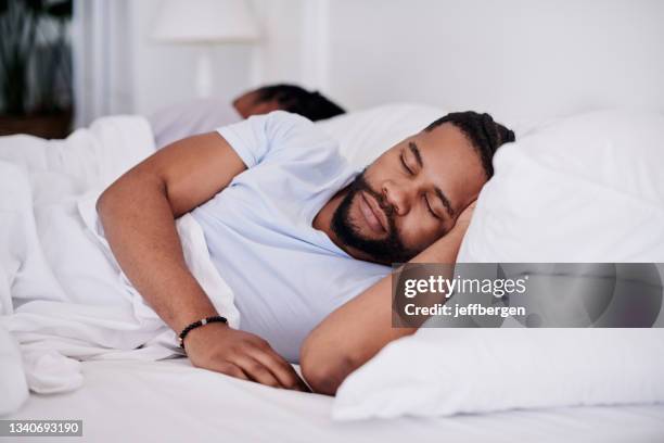 foto de un apuesto joven durmiendo en su cama en casa mientras su novia yace detrás de él - young black girlfriends fotografías e imágenes de stock