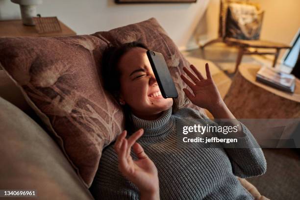 shot of a young woman lying on the couch after her phone fell on her face - bad luck 個照片及圖片檔