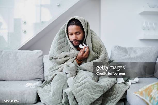 shot of a young man with the flu sitting on the couch at home - illness stock pictures, royalty-free photos & images