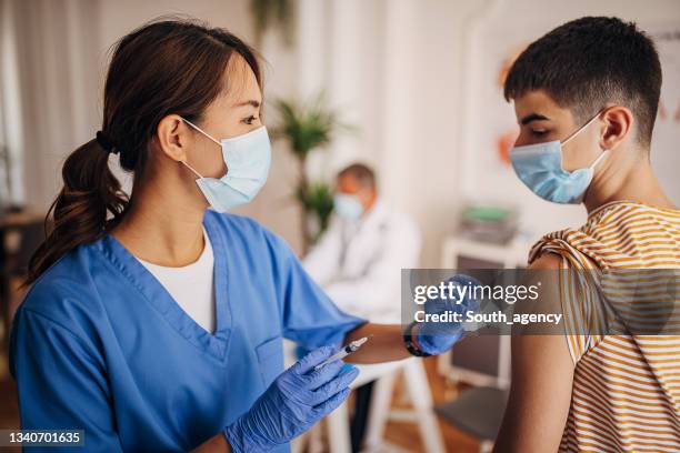 female nurse giving covid-19 vaccine to young teenager at the vaccination center - immunization certificate stock pictures, royalty-free photos & images