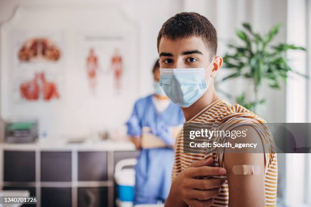 portrait of teenager patient with band aid on his arm after receiving covid-19 vaccine - young adult vaccine stock pictures, royalty-free photos & images