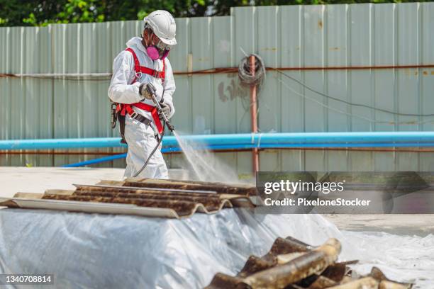 safety is our top priority. worker wearing full body protective clothing while working with the asbestos roof tiles. - asbestos removal photos et images de collection