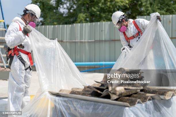 safety is our top priority. workers wearing full body protective clothing while working with the asbestos roof tiles. - asbestos removal stock-fotos und bilder