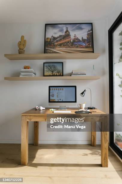 interior of modern workspace with personal computer on wooden desktop and bookshelves above desk locating near big glass wall in light trendy living room at home - coffee table stock photos et images de collection