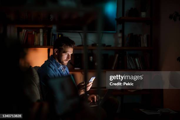 handsome man using phone in his apartment late night - dark living room stock pictures, royalty-free photos & images