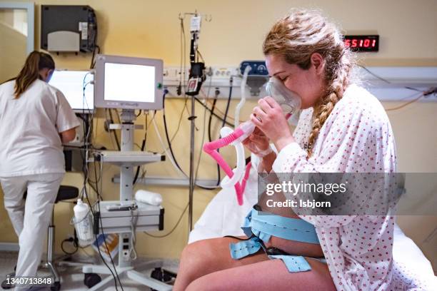 side view of woman sitting on hospital bed during childbirth and using gas mask. - labor childbirth stockfoto's en -beelden