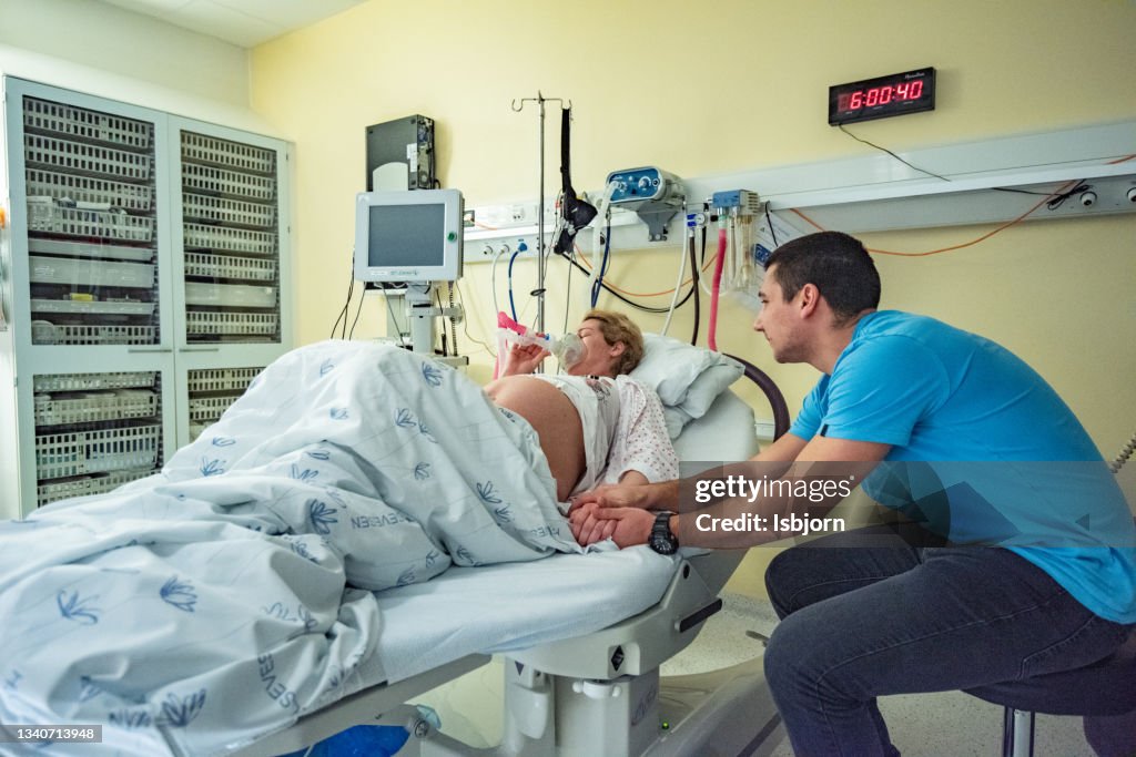 Future mother using respiratory mask in delivery room while her husband holding her hand.